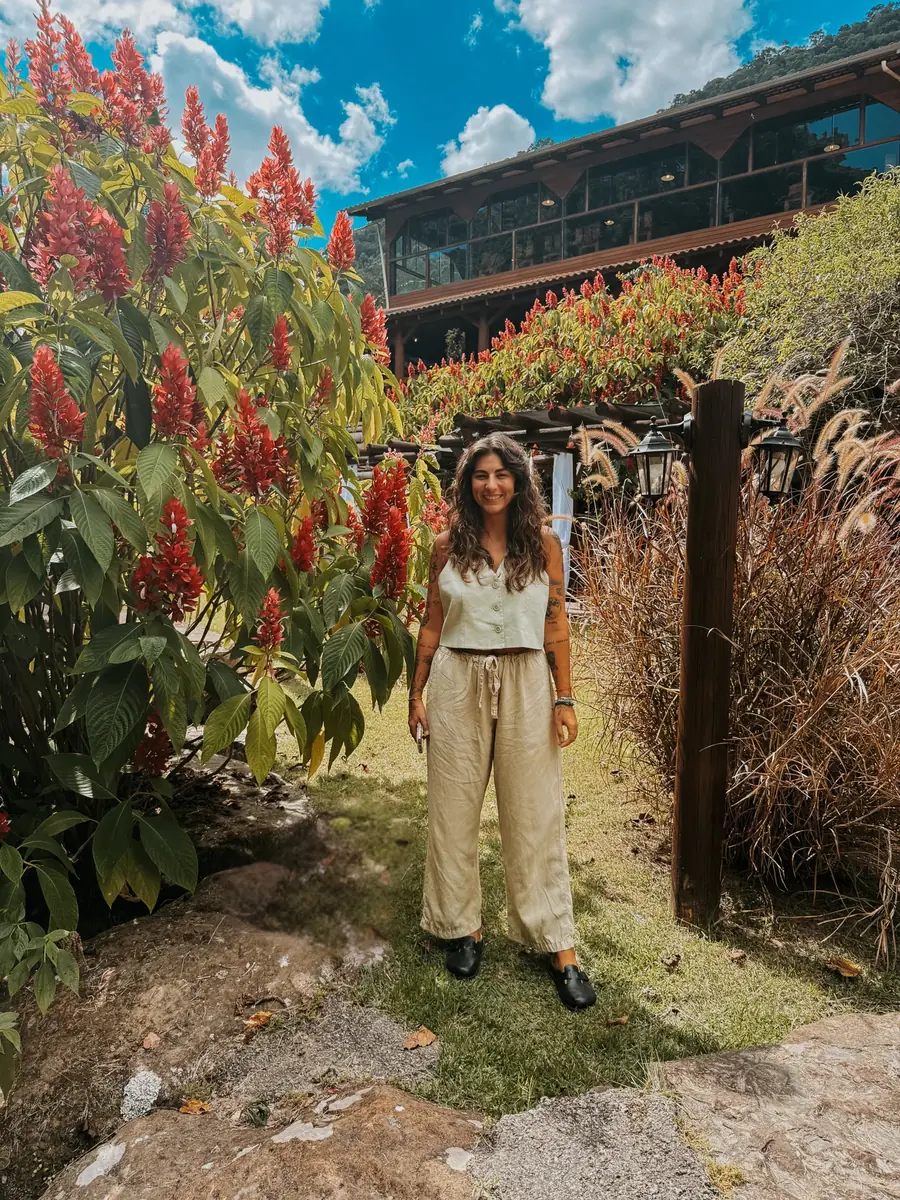 Sarah Abura em um jardim, em frente a uma casa de madeira